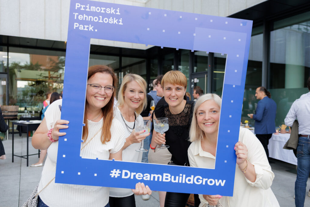 Udeleženke dogodka z nasmeški pozirajo skozi okvir z napisom #DreamBuildGrow.