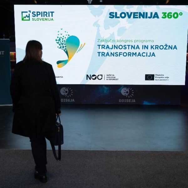 Zaslon z grafiko Zaključnega kongresa TKT in oseba ki hodi proti zaslonu